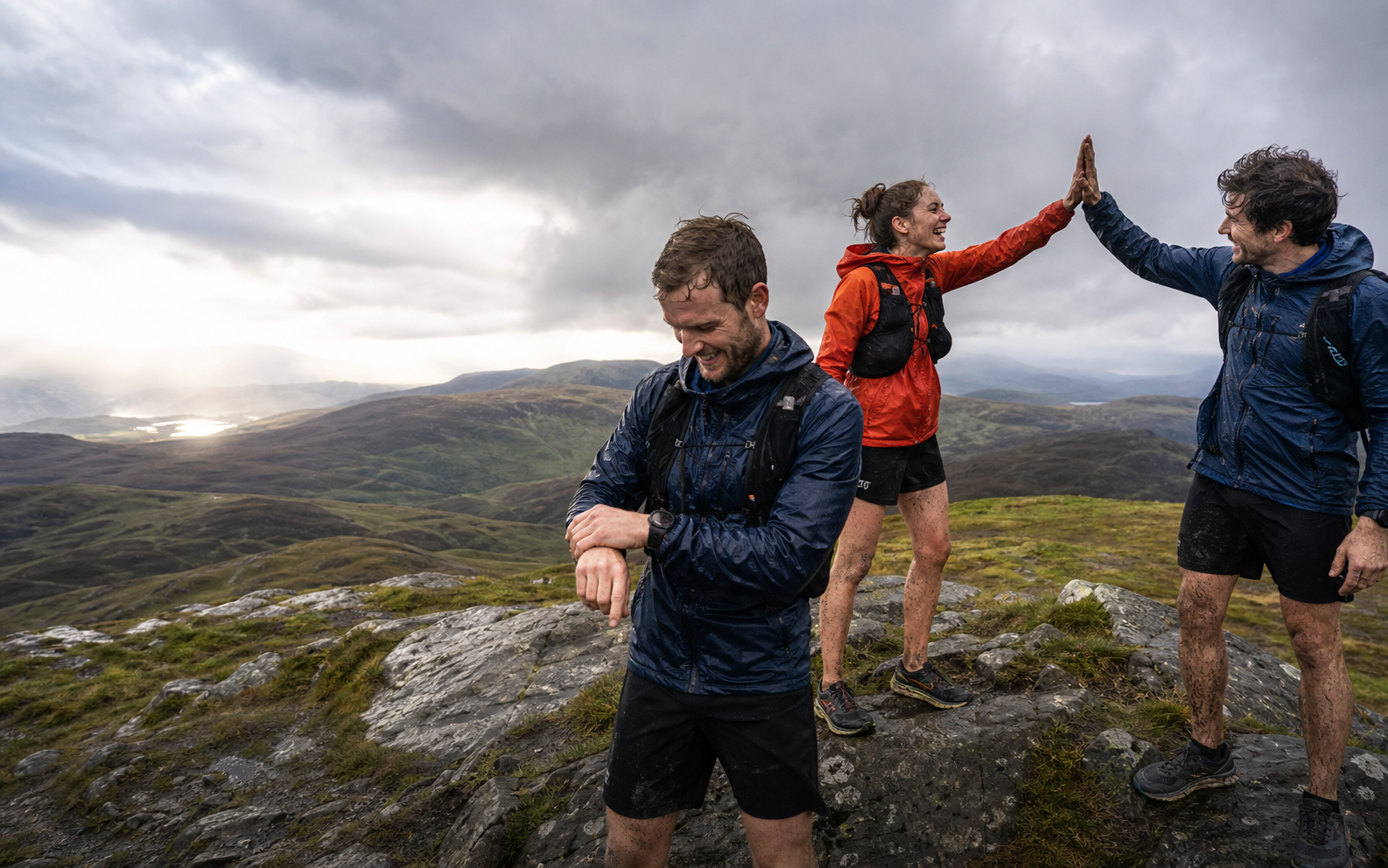 Three muddy hillgoers celebrating together on a Scottish summit while one checks their watch